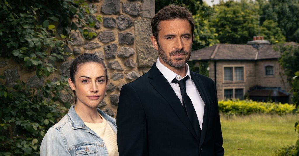 Victoria and John Sugden stand side-by-side looking serious (Credit: ITV)