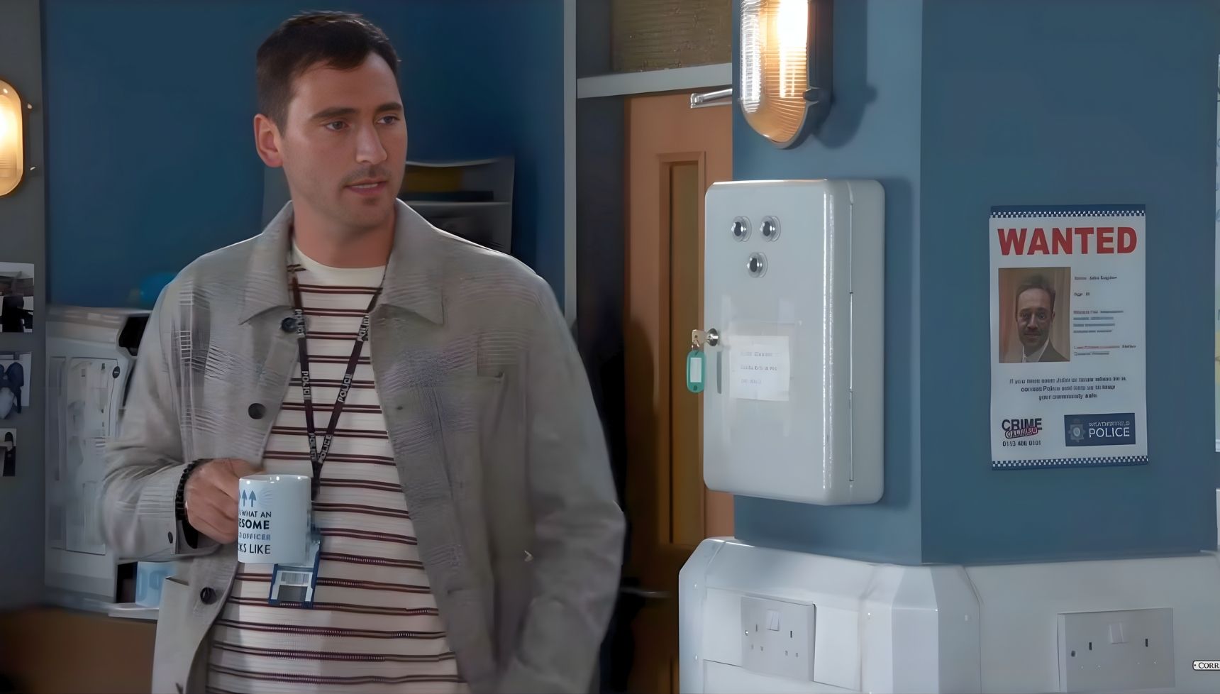 Kit Green in Coronation Street drinks tea next to John's wanted poster (Credit: ITV)